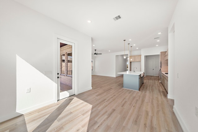 kitchen with a center island with sink, sink, ceiling fan, light wood-type flooring, and decorative light fixtures