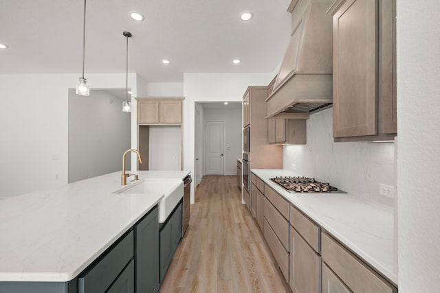 kitchen with sink, decorative light fixtures, a kitchen island with sink, custom range hood, and light wood-type flooring