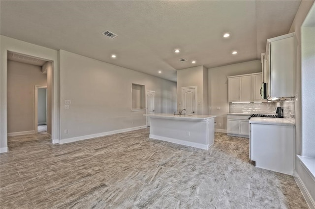 kitchen featuring white cabinets, backsplash, an island with sink, stove, and sink