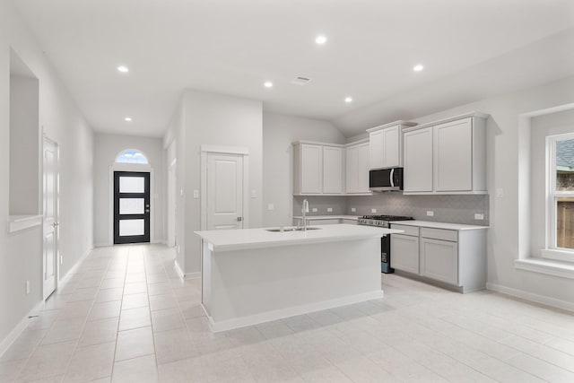 kitchen featuring sink, appliances with stainless steel finishes, gray cabinets, an island with sink, and decorative backsplash