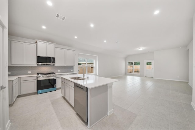 kitchen featuring gray cabinets, appliances with stainless steel finishes, sink, decorative backsplash, and a kitchen island with sink