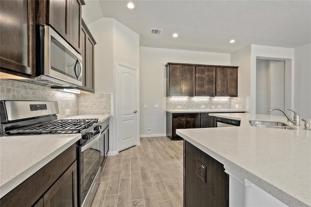 kitchen with tasteful backsplash, appliances with stainless steel finishes, dark brown cabinets, light hardwood / wood-style floors, and light stone counters