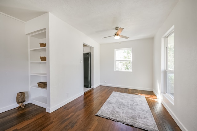 empty room featuring ceiling fan, a textured ceiling, built in features, and dark hardwood / wood-style flooring