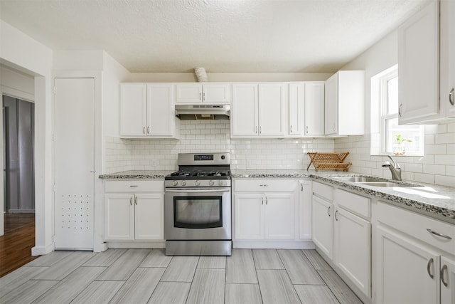 kitchen with white cabinets, tasteful backsplash, light stone countertops, stainless steel range with gas cooktop, and sink