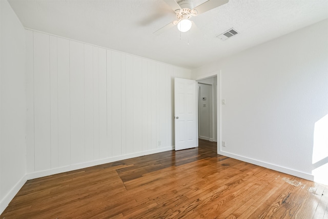 spare room featuring wood walls, hardwood / wood-style floors, a textured ceiling, and ceiling fan