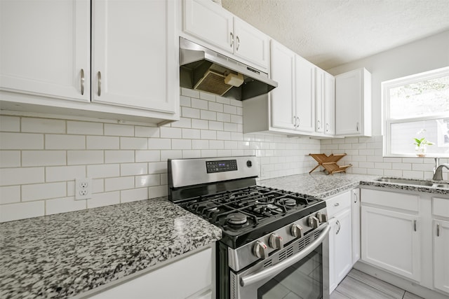 kitchen featuring backsplash, sink, light stone countertops, stainless steel gas range oven, and white cabinets