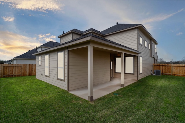 back of property at dusk featuring central AC unit, a lawn, a patio area, and a fenced backyard