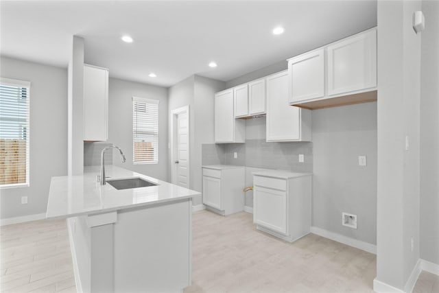 kitchen featuring light wood finished floors, white cabinets, a sink, light countertops, and backsplash