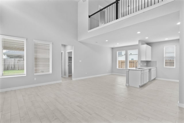 unfurnished living room featuring light wood finished floors, recessed lighting, a towering ceiling, a sink, and baseboards