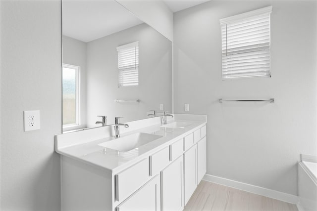 full bath featuring a tub to relax in, a sink, baseboards, and double vanity