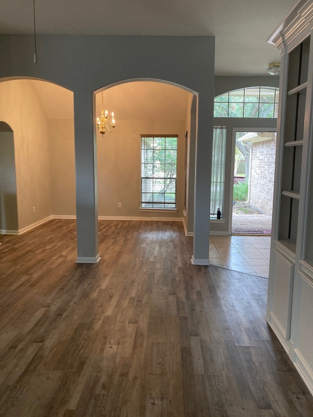 empty room with a notable chandelier, a healthy amount of sunlight, and dark hardwood / wood-style flooring