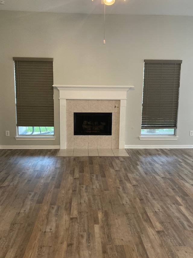 unfurnished living room with a tile fireplace, dark hardwood / wood-style flooring, and ceiling fan