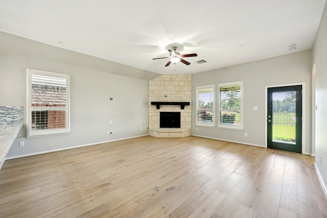 unfurnished living room with ceiling fan, a stone fireplace, vaulted ceiling, and light hardwood / wood-style flooring