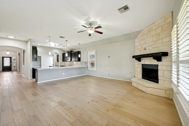 unfurnished living room featuring a stone fireplace, ceiling fan, and light hardwood / wood-style flooring