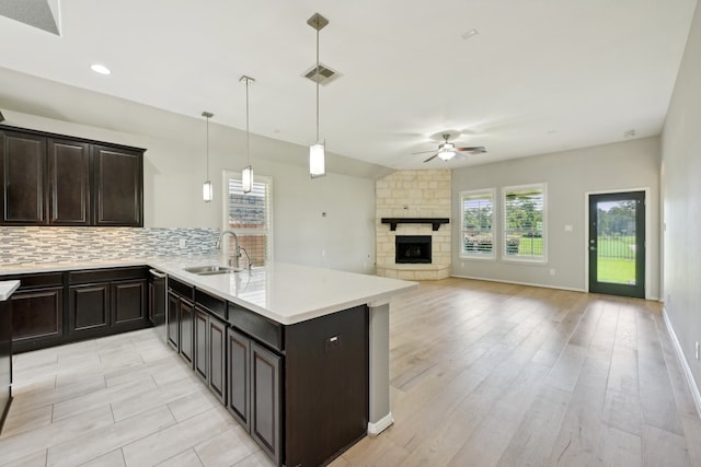 kitchen with sink, light hardwood / wood-style flooring, hanging light fixtures, a fireplace, and backsplash