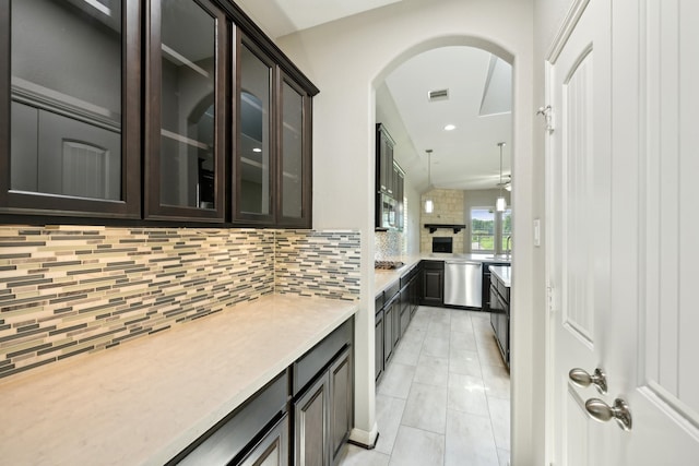 kitchen featuring light tile patterned flooring, dark brown cabinetry, decorative light fixtures, stainless steel appliances, and backsplash