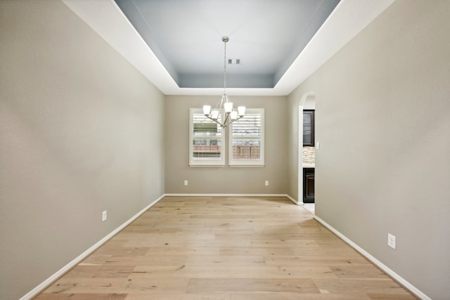 unfurnished dining area with light hardwood / wood-style flooring, an inviting chandelier, and a tray ceiling