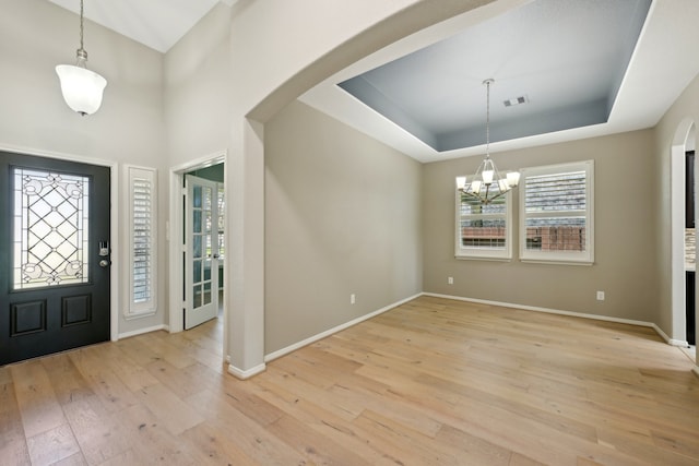 entrance foyer featuring a notable chandelier, a tray ceiling, and light hardwood / wood-style floors