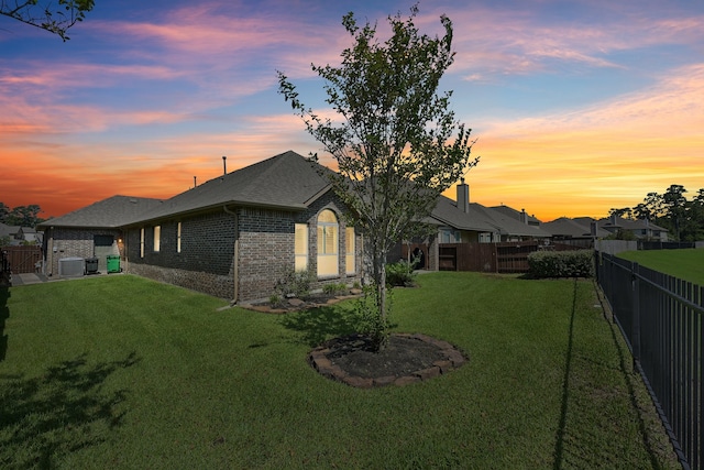 back house at dusk with central AC and a lawn