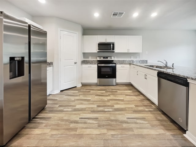 kitchen featuring white cabinets, light wood-type flooring, light stone countertops, stainless steel appliances, and sink