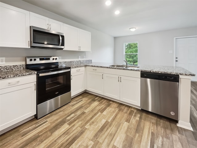 kitchen with light hardwood / wood-style flooring, stainless steel appliances, sink, kitchen peninsula, and light stone counters