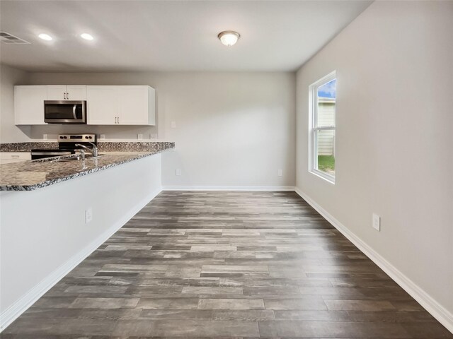 kitchen with appliances with stainless steel finishes, white cabinetry, hardwood / wood-style flooring, and stone counters