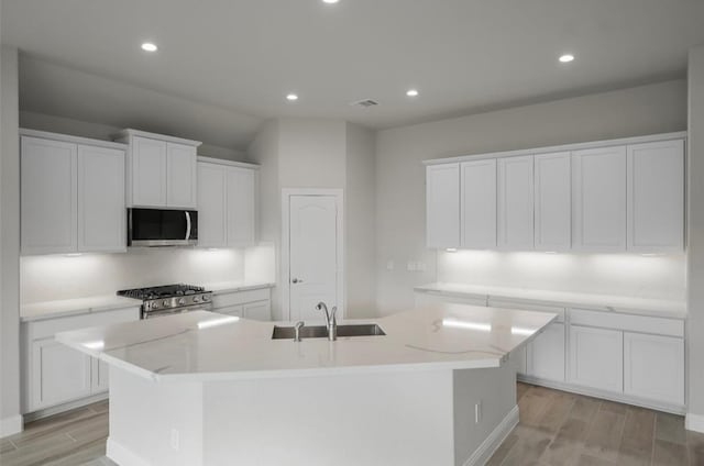 kitchen featuring stainless steel appliances, light hardwood / wood-style floors, a kitchen island with sink, and white cabinetry