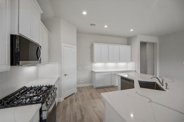 kitchen with white cabinetry, light stone counters, sink, appliances with stainless steel finishes, and light hardwood / wood-style floors