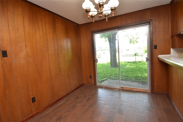 unfurnished dining area with a textured ceiling, wooden walls, dark hardwood / wood-style flooring, and a chandelier