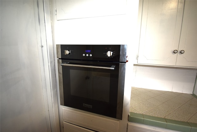 interior space featuring black oven, tile counters, and white cabinetry