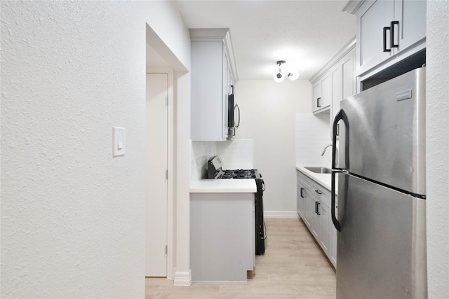 kitchen with light wood-type flooring, tasteful backsplash, stainless steel appliances, sink, and white cabinets