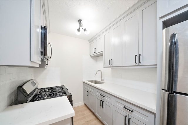 kitchen with a textured ceiling, appliances with stainless steel finishes, tasteful backsplash, light hardwood / wood-style floors, and sink