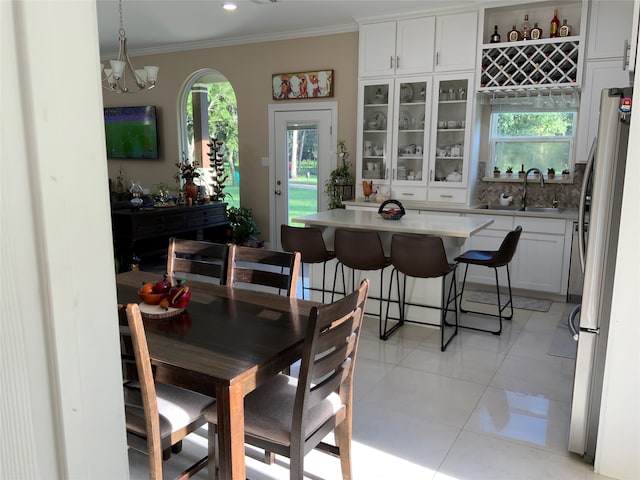 tiled dining area with an inviting chandelier, crown molding, and sink