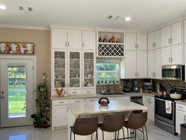 kitchen featuring a kitchen breakfast bar, backsplash, appliances with stainless steel finishes, sink, and white cabinetry