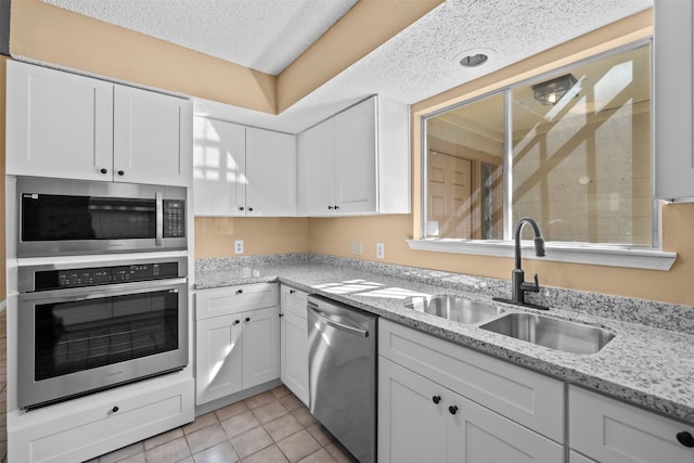 kitchen with light stone countertops, light tile patterned floors, stainless steel appliances, sink, and white cabinetry