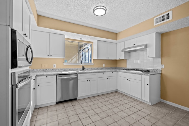 kitchen with appliances with stainless steel finishes, white cabinetry, light stone counters, and backsplash