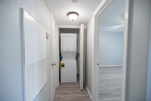 hallway featuring light wood-type flooring, stacked washer and clothes dryer, and a textured ceiling