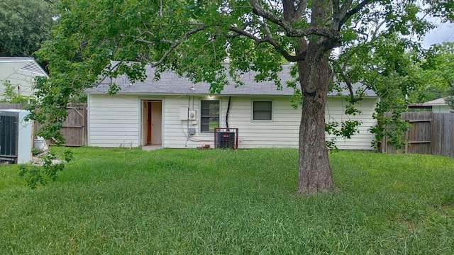 rear view of property featuring central AC unit and a lawn