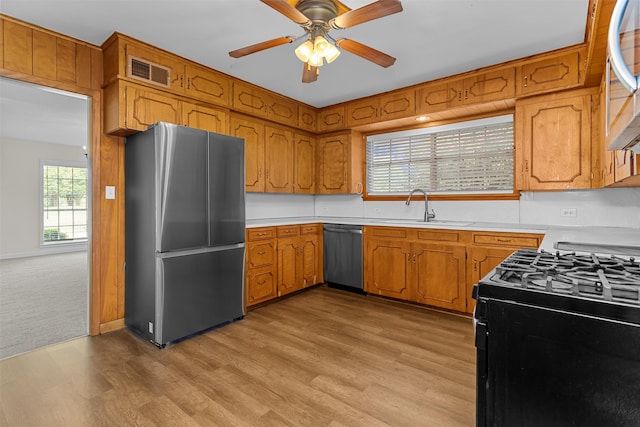 kitchen with light wood-type flooring, appliances with stainless steel finishes, sink, and ceiling fan