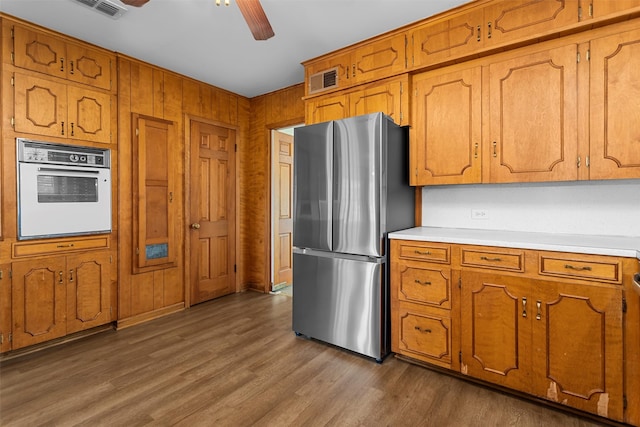 kitchen with dark hardwood / wood-style floors, wood walls, white oven, stainless steel fridge, and ceiling fan