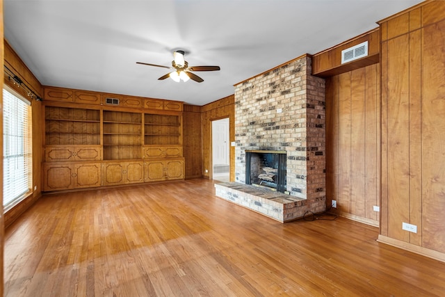 unfurnished living room with a healthy amount of sunlight, a brick fireplace, wood walls, and ceiling fan