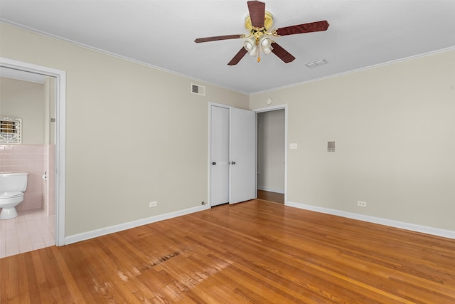 unfurnished bedroom with crown molding, ensuite bath, ceiling fan, tile walls, and light hardwood / wood-style floors