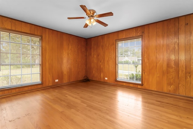 empty room featuring ceiling fan, light wood-type flooring, and wooden walls