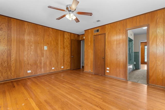 unfurnished bedroom with wood walls, light hardwood / wood-style flooring, ensuite bathroom, and ceiling fan