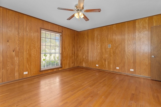 empty room with ceiling fan, wood walls, and light hardwood / wood-style floors