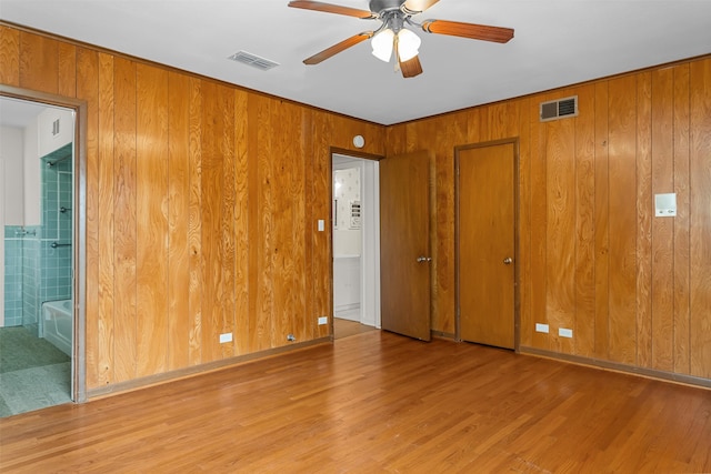 unfurnished bedroom with ceiling fan, wooden walls, light hardwood / wood-style floors, and ensuite bath