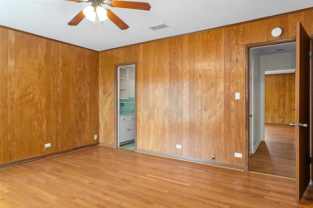 unfurnished bedroom featuring wood walls, wood-type flooring, connected bathroom, and ceiling fan