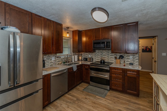 kitchen featuring a textured ceiling, appliances with stainless steel finishes, tasteful backsplash, sink, and light wood-type flooring