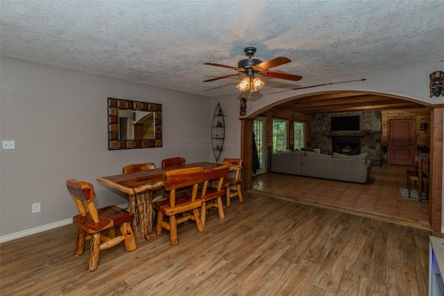 dining space with a textured ceiling, beamed ceiling, a fireplace, wood-type flooring, and ceiling fan