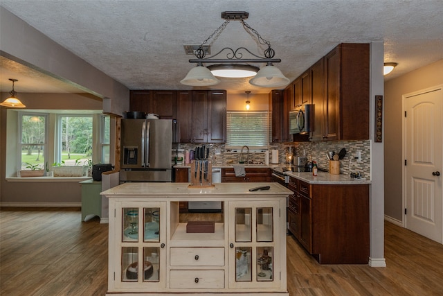 kitchen with light wood-type flooring, pendant lighting, stainless steel appliances, and a textured ceiling